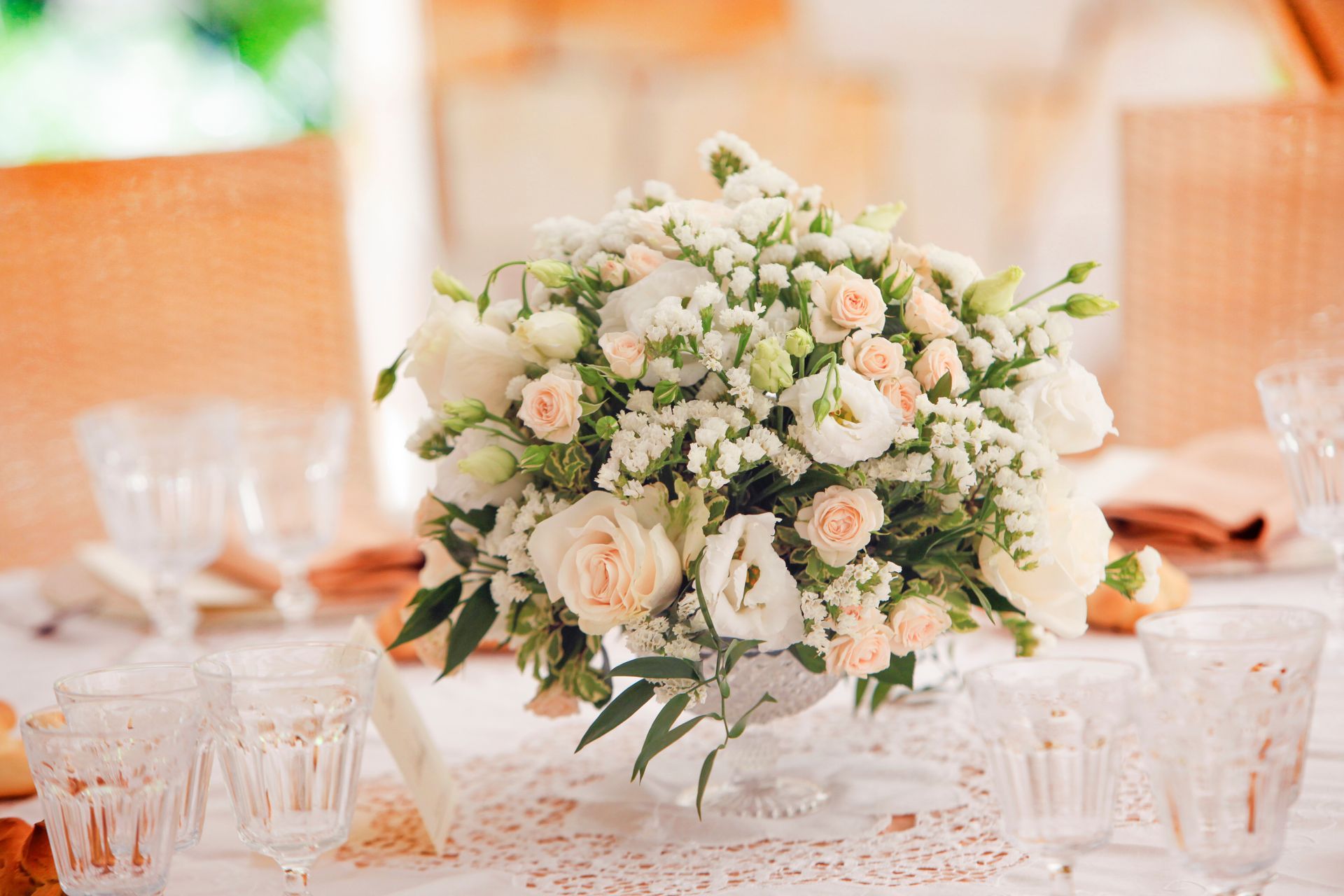 Centre de table floral blanc et rose poudré sur une table à manger décorée avec de la verrerie et des chaises orange chaud.