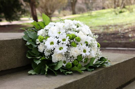 Bouquet de fleurs blanches aux feuilles vertes posé sur des marches en pierre à l'extérieur.