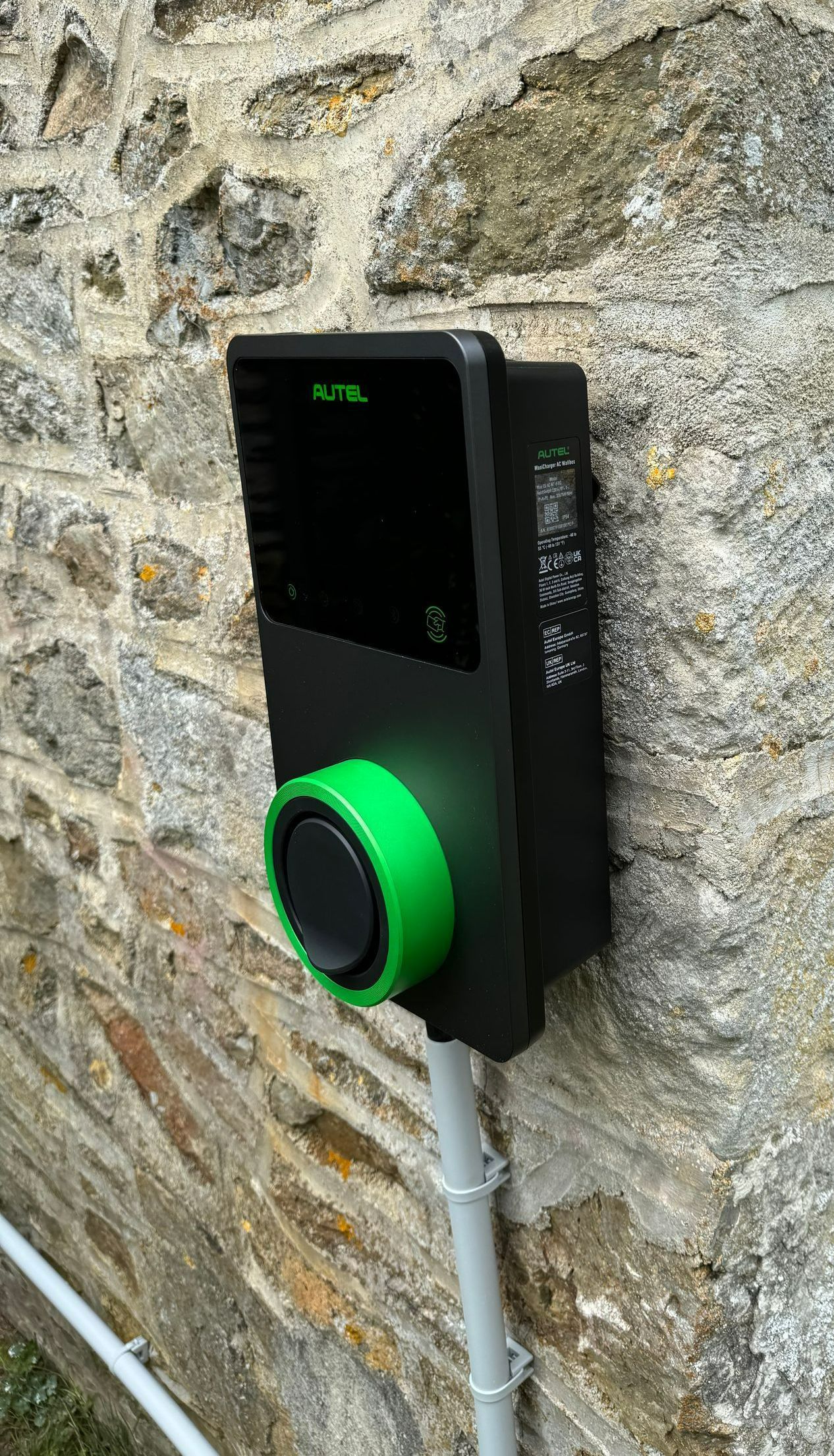 Une borne de recharge verte et noire installée près de l'angle d'un mur