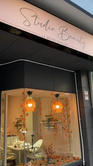 Fachada con letrero rosa de “Studio Beauty”, fachada negra y escaparate iluminado con luz naranja cálida.