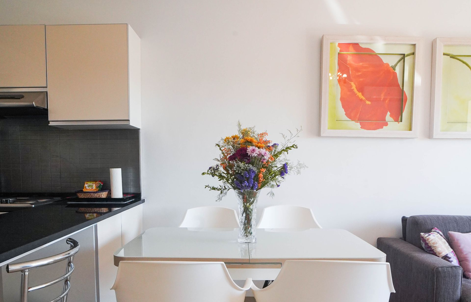 Small kitchen with dining table and colorful flower bouquet. Artwork on wall, gray couch.