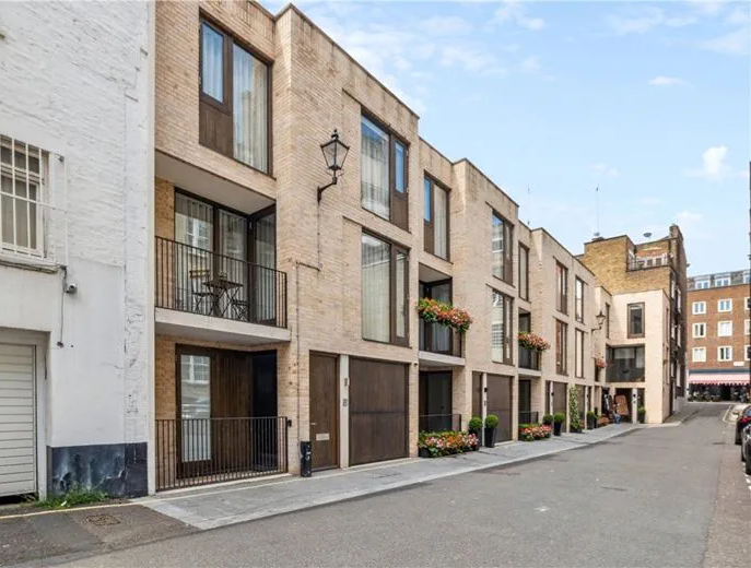 Row of modern brick townhouses with balconies, garages, and street in London.