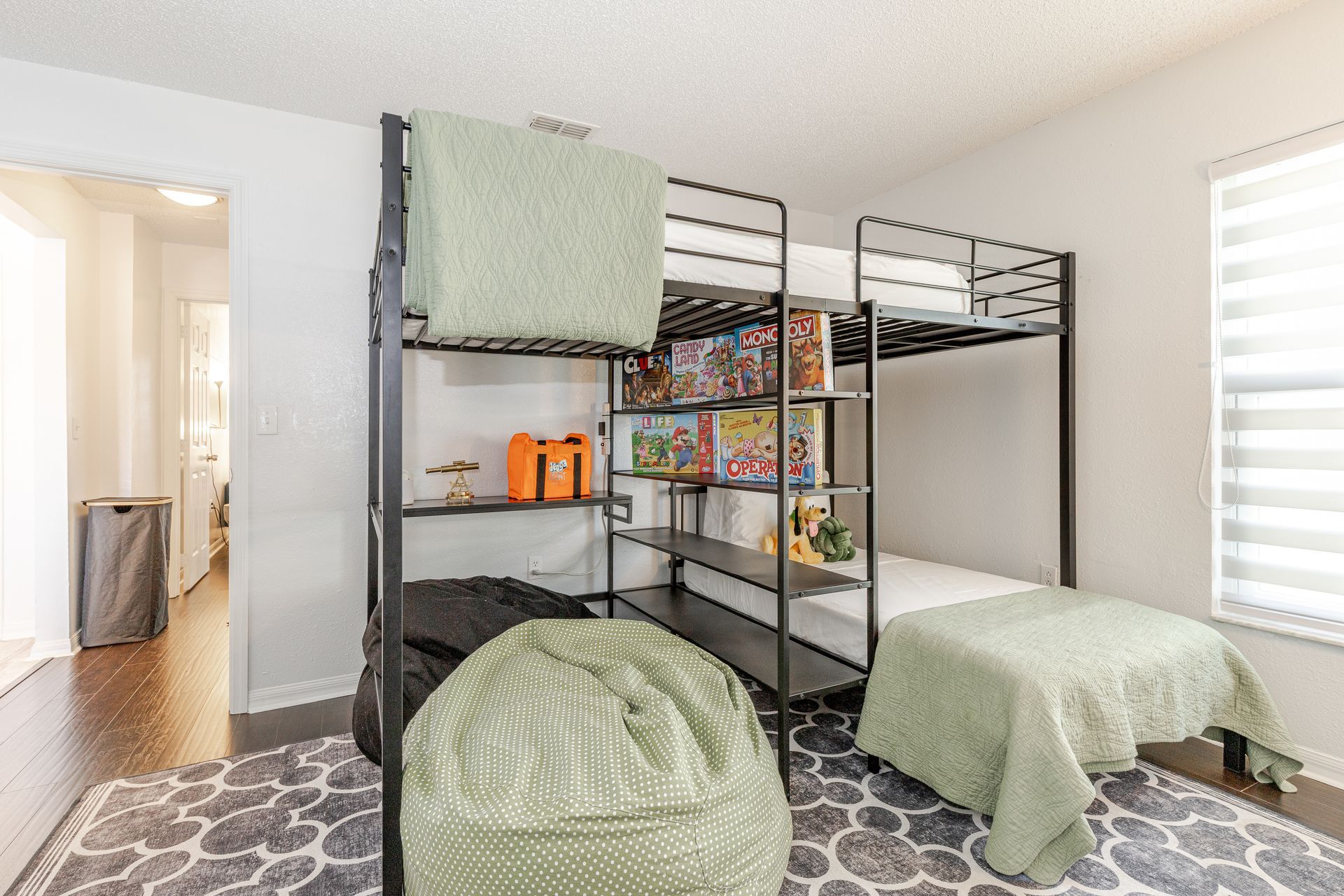 A child's bedroom with a black metal bunk bed, shelving, and a patterned rug.