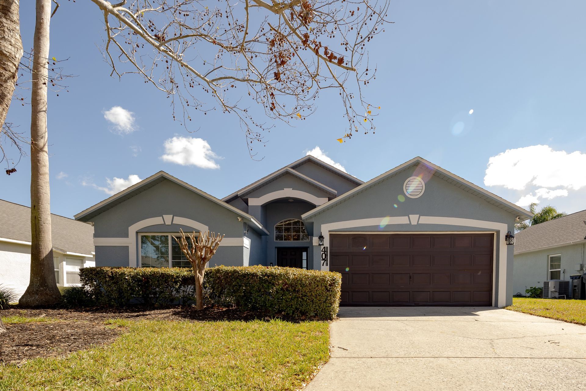 Blue-gray house with brown garage door, green lawn, and sunny blue sky.