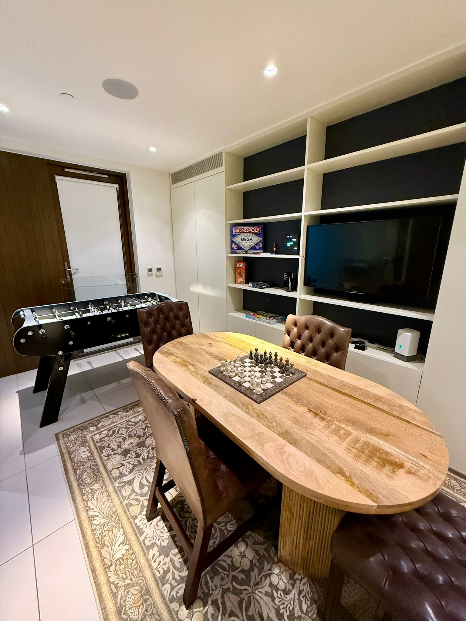 Game room with foosball table, chess table, and built-in shelving with TV.