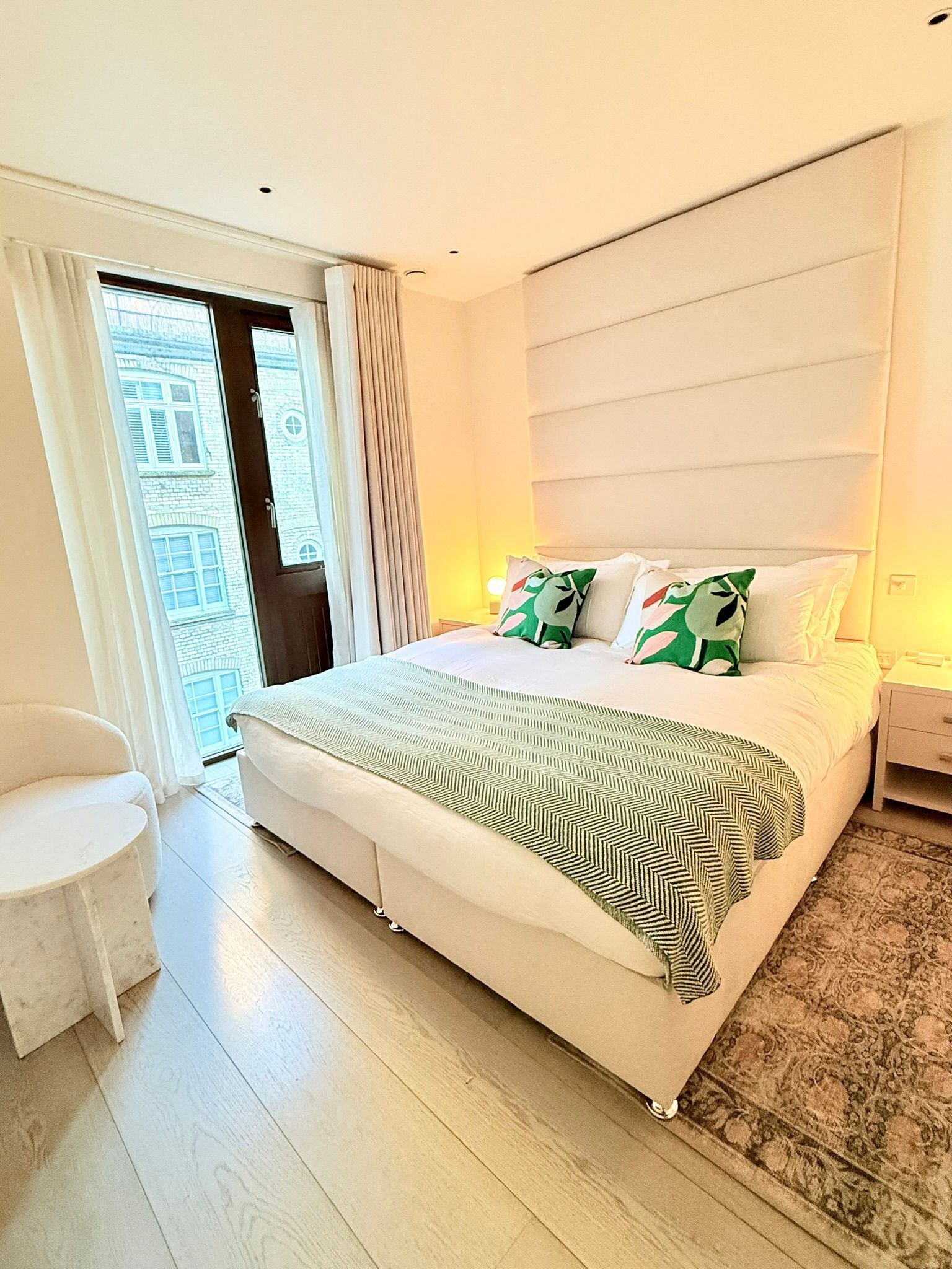 Bedroom with large bed, balcony door, white and green accents, and a rug.