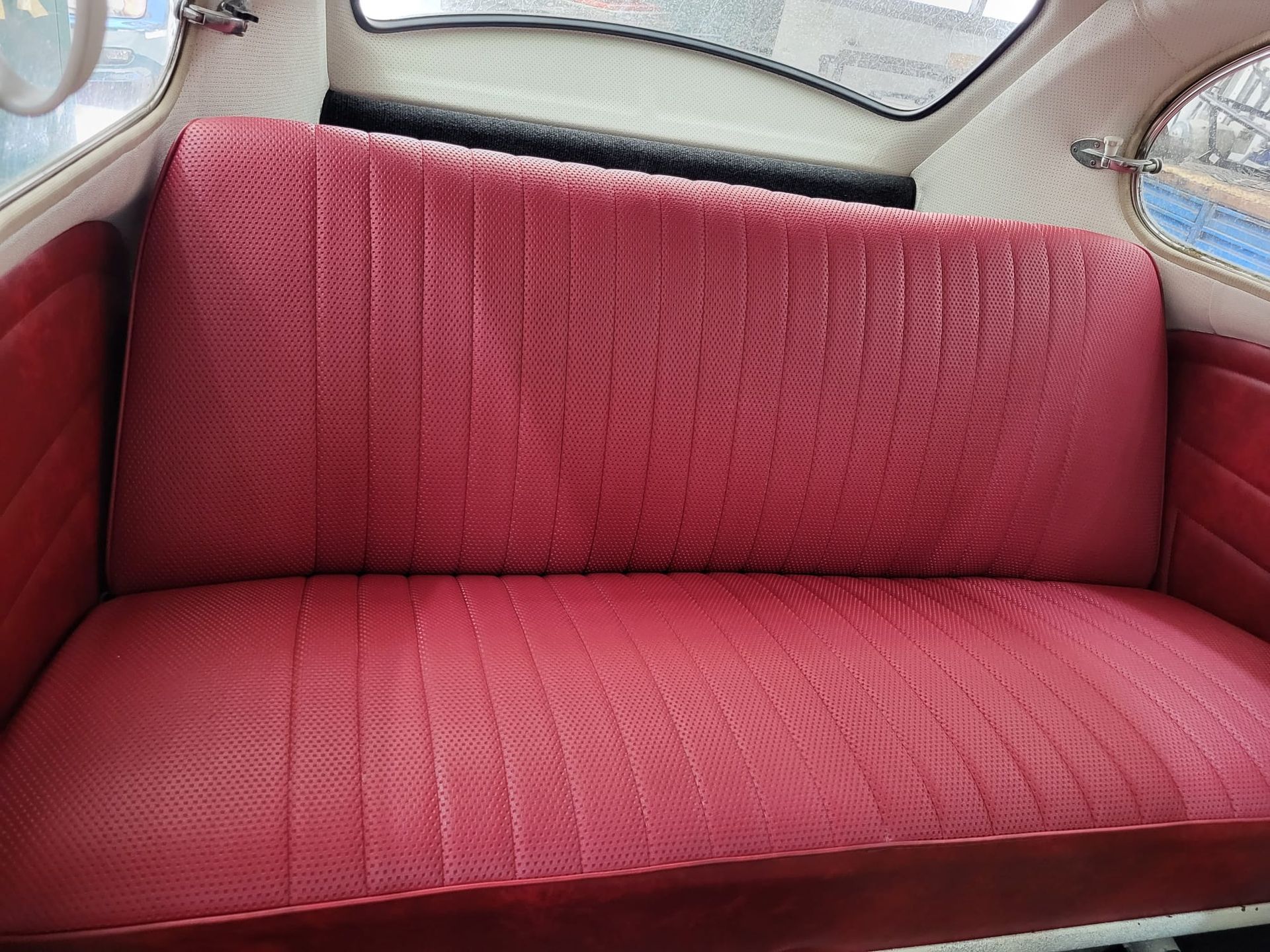 Banco tapizado en rojo en el interior de un coche clásico con ventana trasera curva.