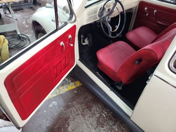 Interior clásico de coche blanco con puerta abierta, panel de puerta rojo y asientos rojos.