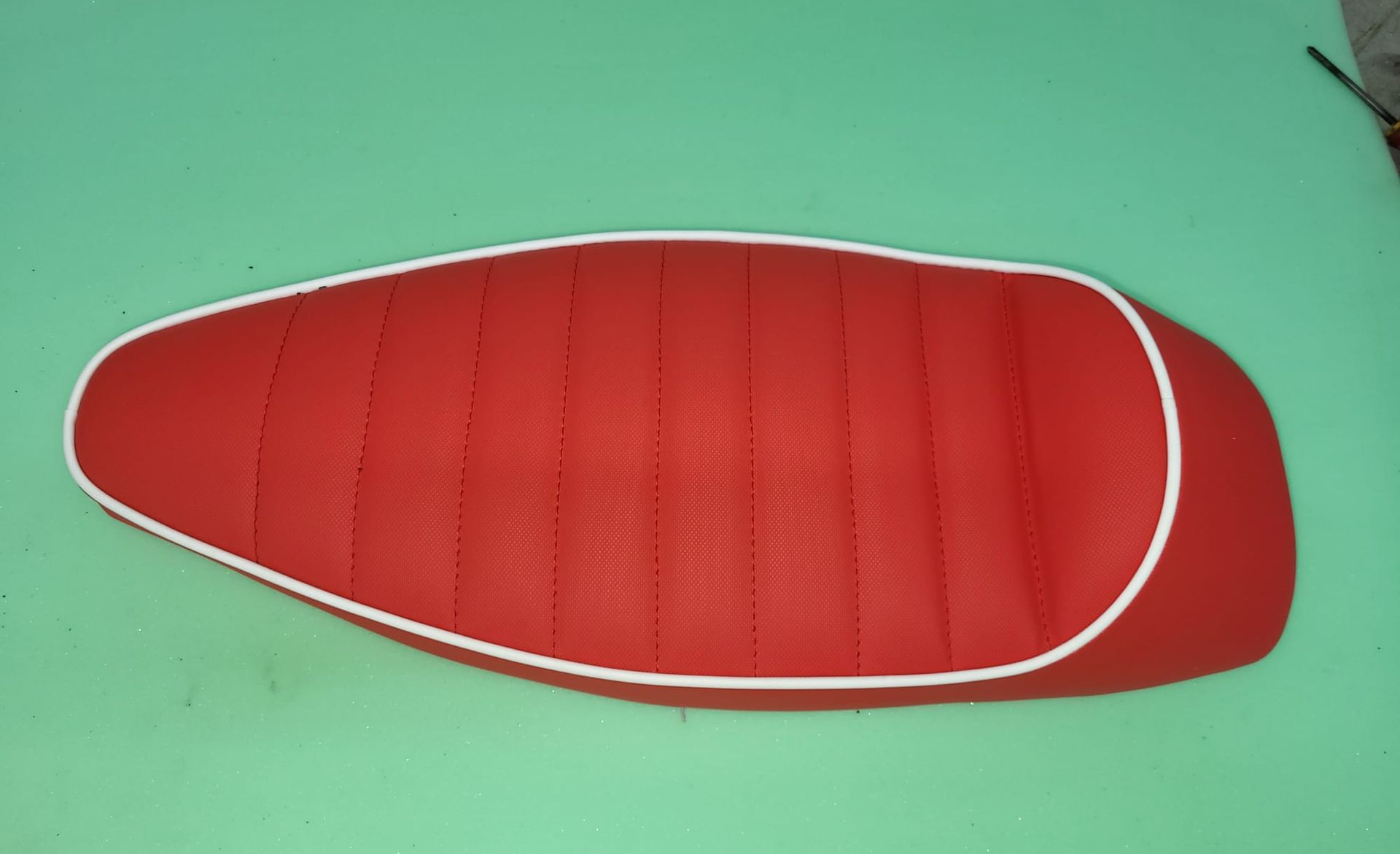 Asiento o cojín acolchado rojo y blanco con forma de pan sobre una superficie verde.
