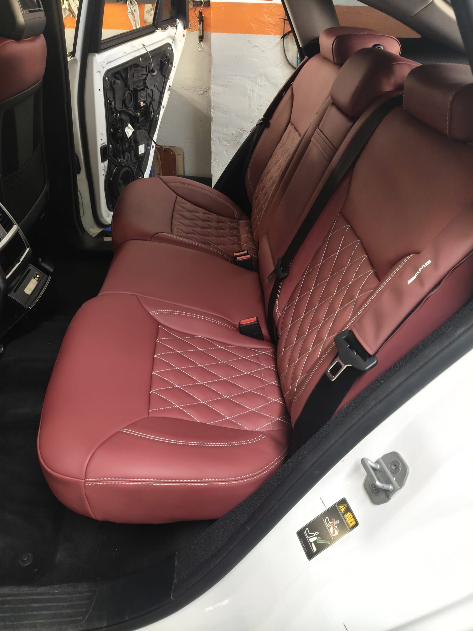 Asiento trasero de coche de cuero color granate con costuras acolchadas, visto a través de una puerta trasera abierta.