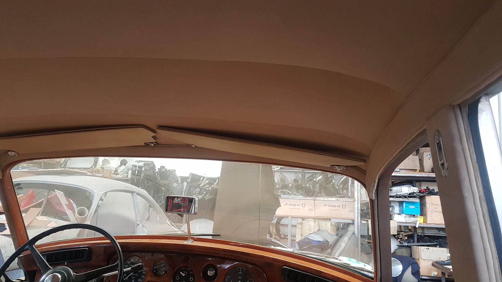 Vista desde el interior de un coche antiguo con salpicadero y parabrisas de madera, con una escena callejera al fondo.