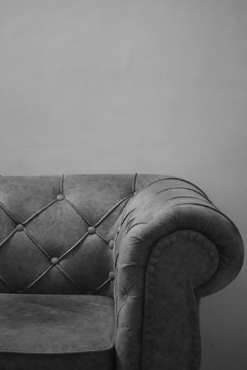 Reposabrazos de sofá gris capitoné contra una pared lisa en una fotografía en blanco y negro.