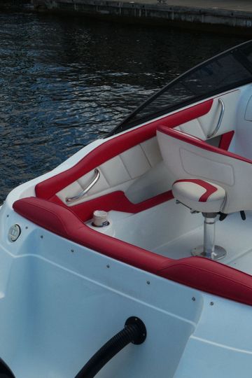 Interior de barco blanco con detalles en rojo y un volante cerca del agua.