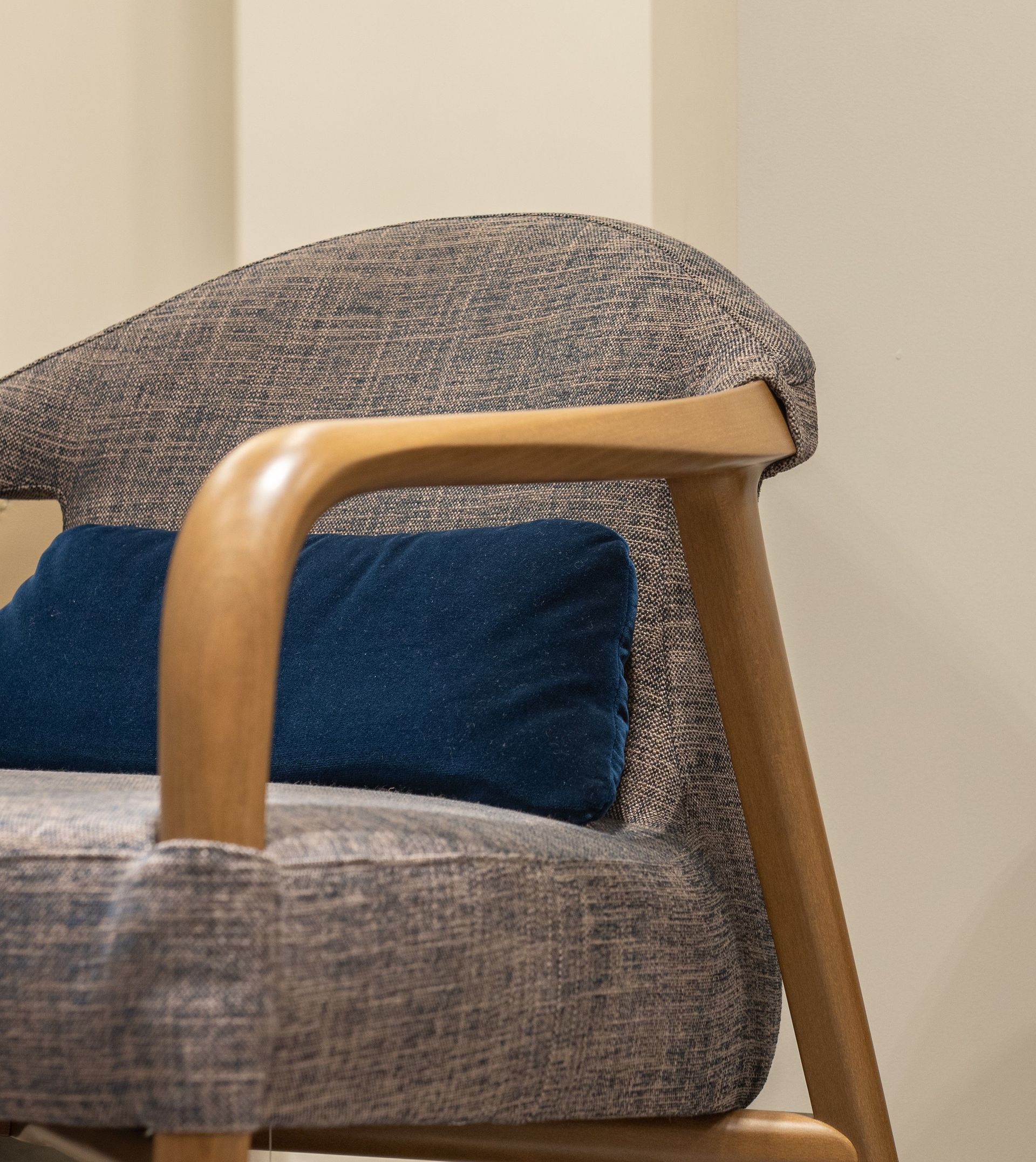 Primer plano de un sillón tapizado en gris con brazos de madera clara y un cojín azul.