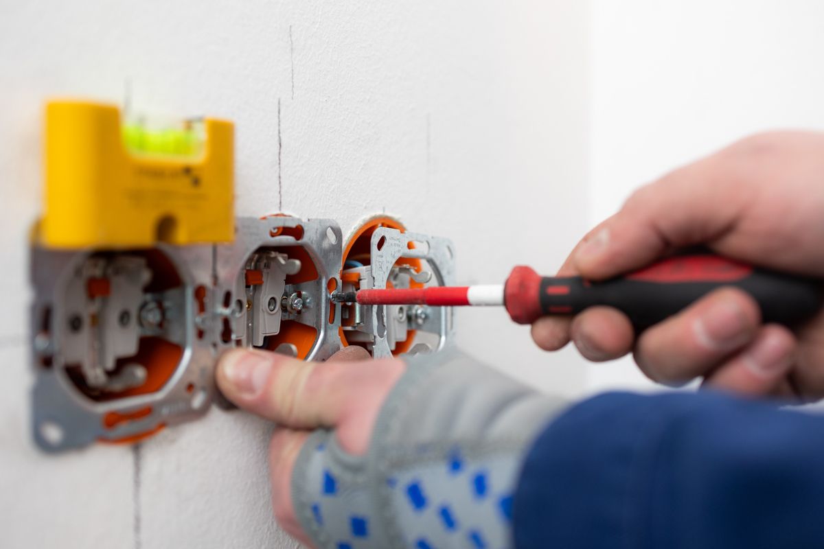 Eine Person befestigt mit einem Schraubenzieher eine Steckdose an einer Wand.