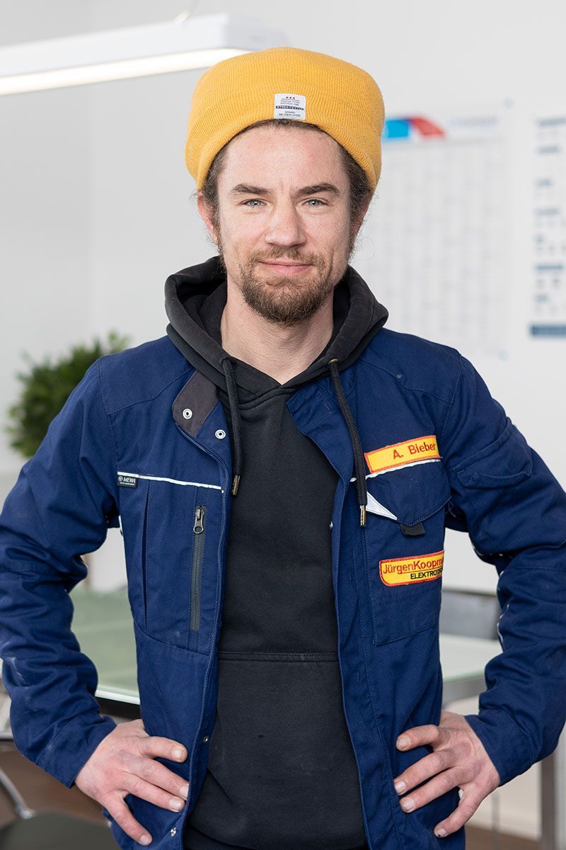 Ein Mann mit einem gelben Hut und einer blauen Jacke steht mit den Händen in den Hüften da.