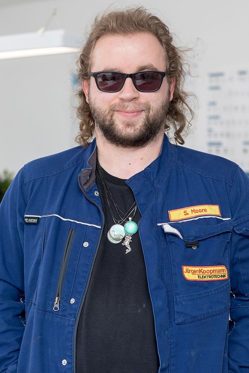 Ein Mann mit Sonnenbrille und blauer Jacke steht in einem Raum.