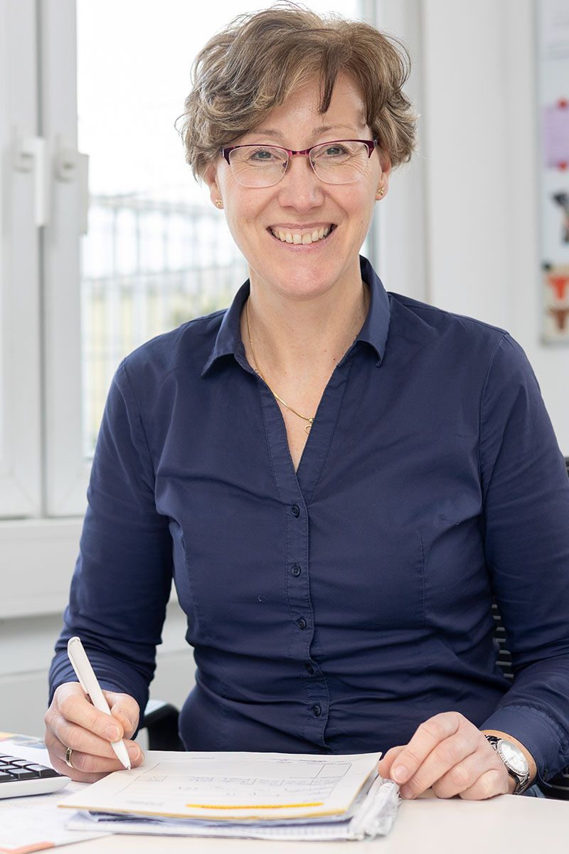 Eine Frau sitzt mit einem Stift in der Hand an einem Schreibtisch.