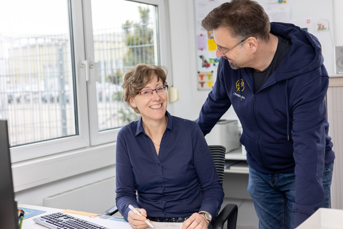 Ein Mann und eine Frau sitzen an einem Schreibtisch vor einem Computer.