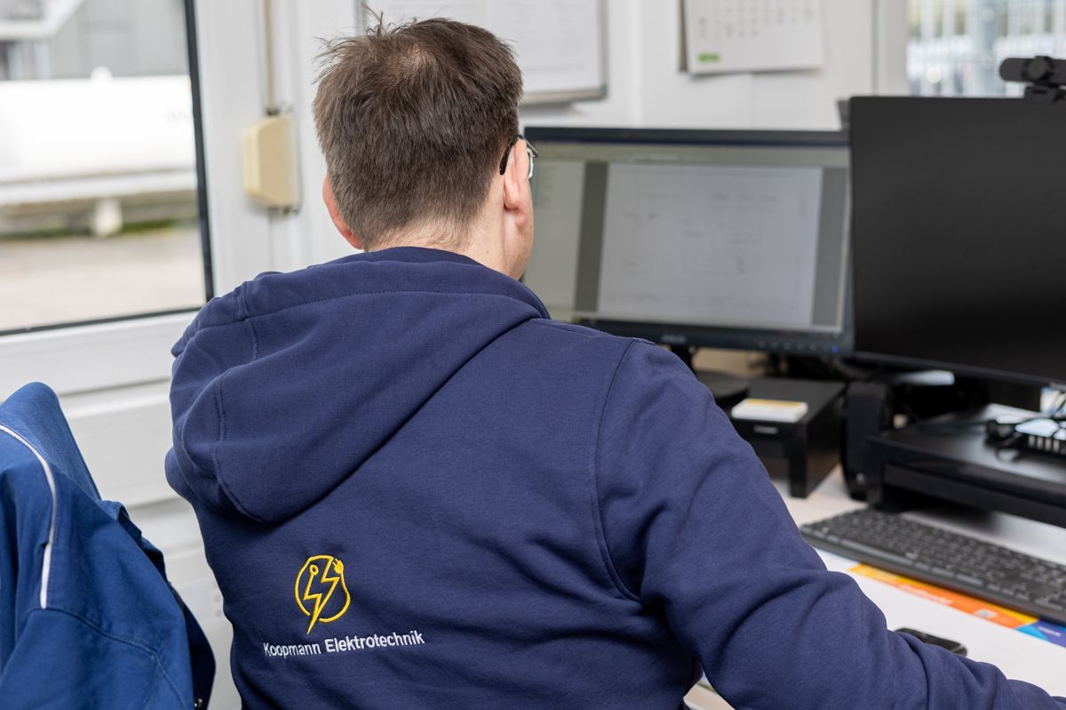 Ein Mann in einem blauen Kapuzenpullover sitzt vor einem Computer.