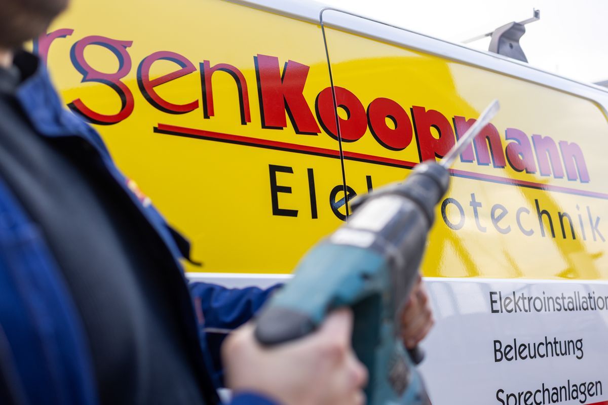 Ein Mann hält eine Bohrmaschine vor einem Lieferwagen mit der Aufschrift Koopmann