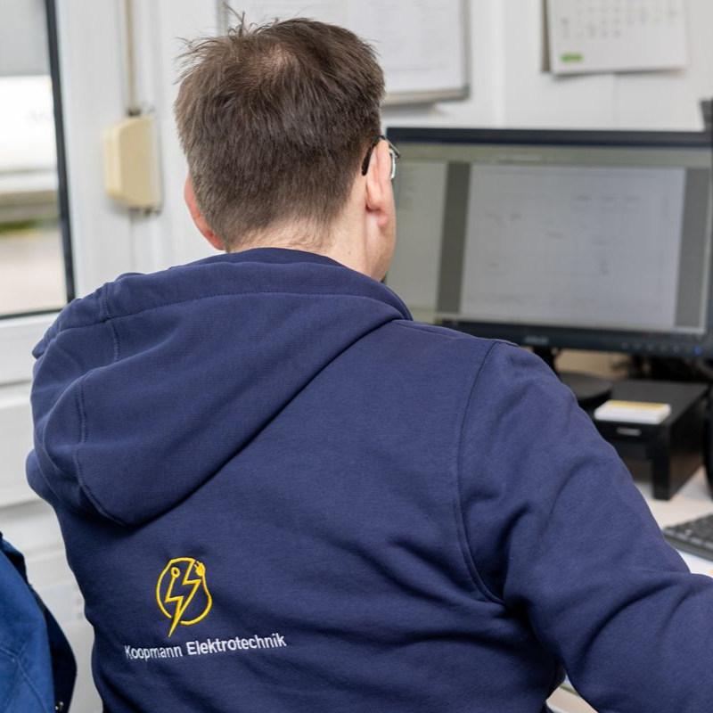 Eine Person in einem blauen Kapuzenpullover arbeitet in einem Büro an einem Computer.