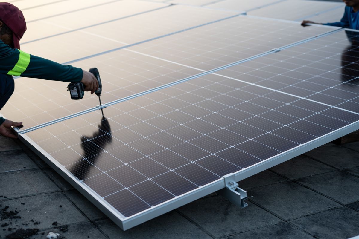 Ein Arbeiter reinigt mit Bürste und Schlauch ein Solarpanel auf einem Dach.