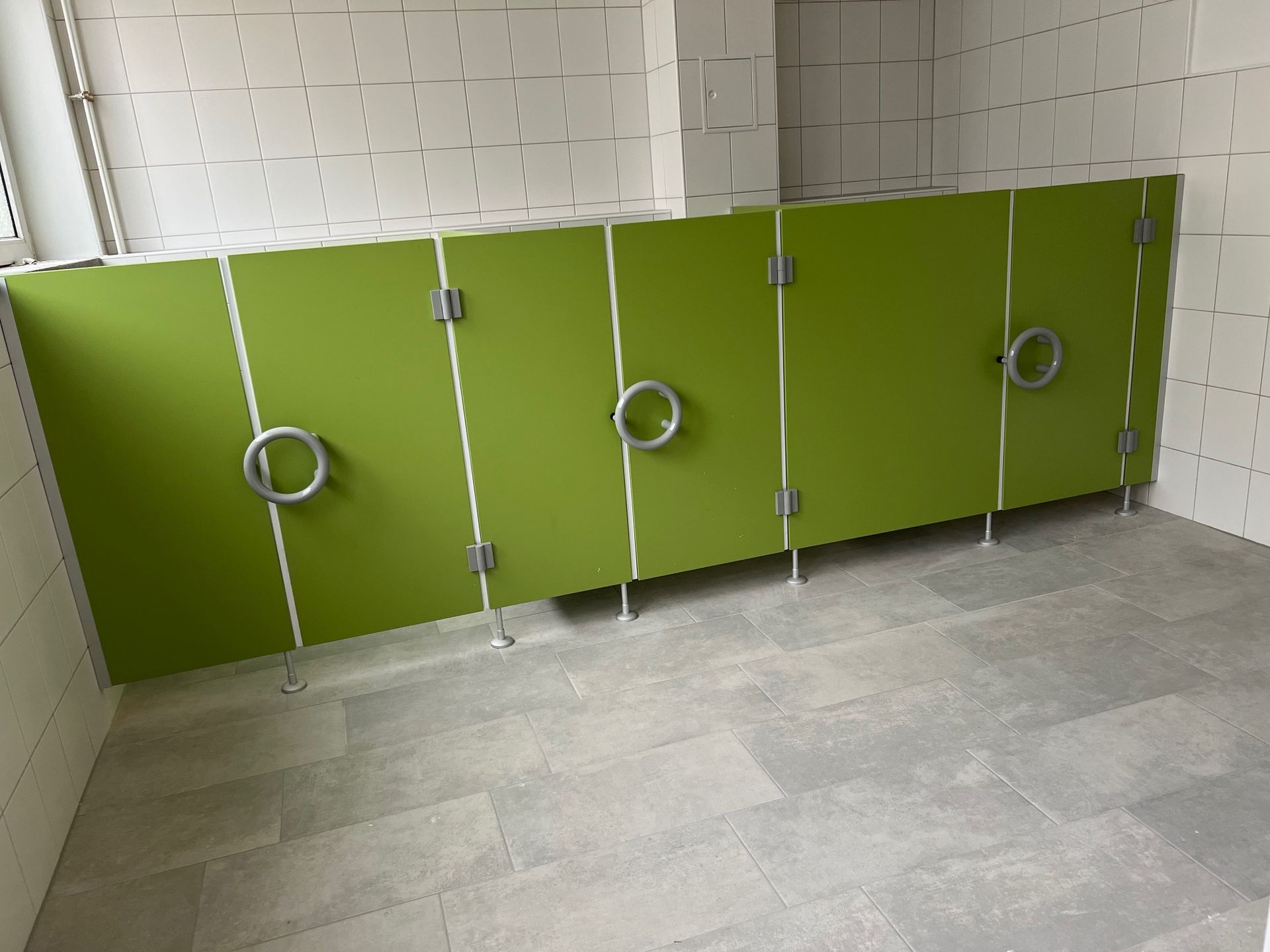 Eine Reihe grüner Toilettenkabinen in einem Badezimmer.