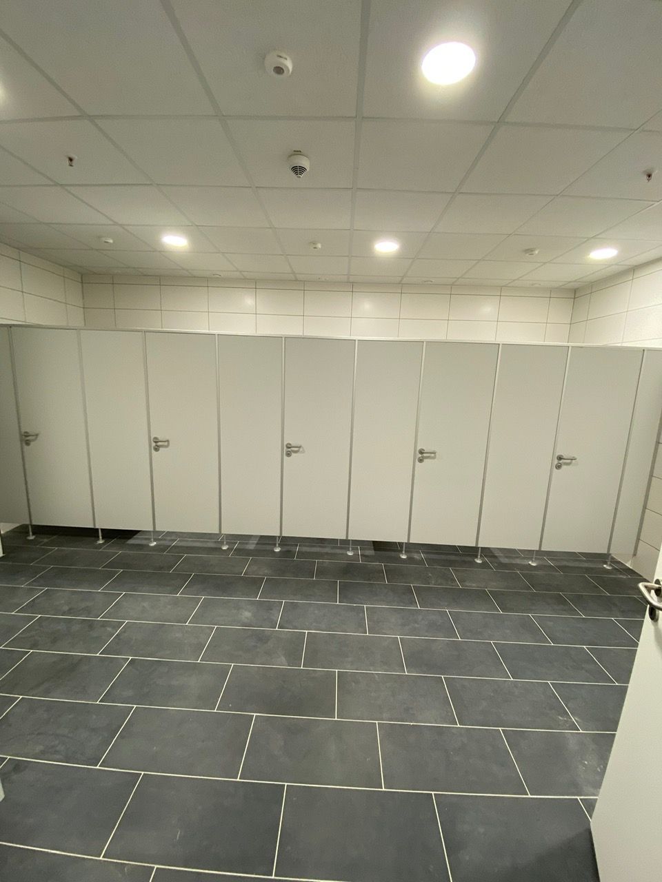 Ein Badezimmer mit gefliestem Boden und weißen Kabinen.