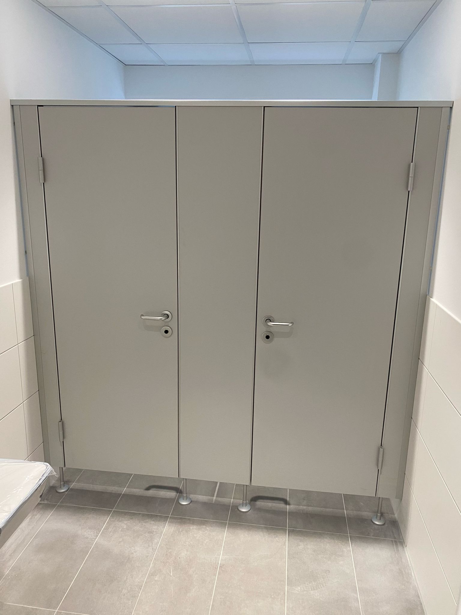 Eine Toilettenkabine mit drei Türen und einem Edelstahlrahmen