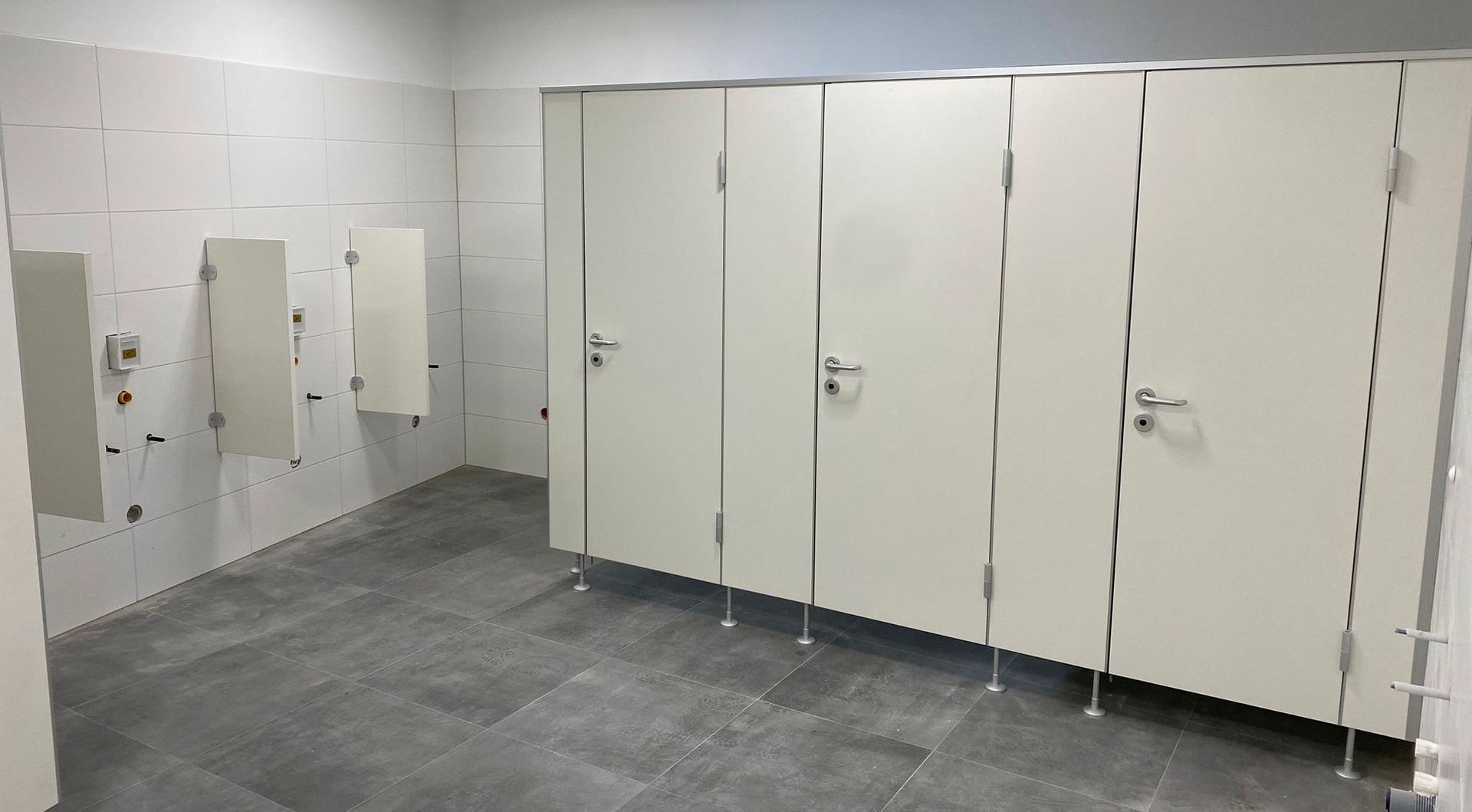 Eine Reihe weißer Toilettenkabinen in einer öffentlichen Toilette.
