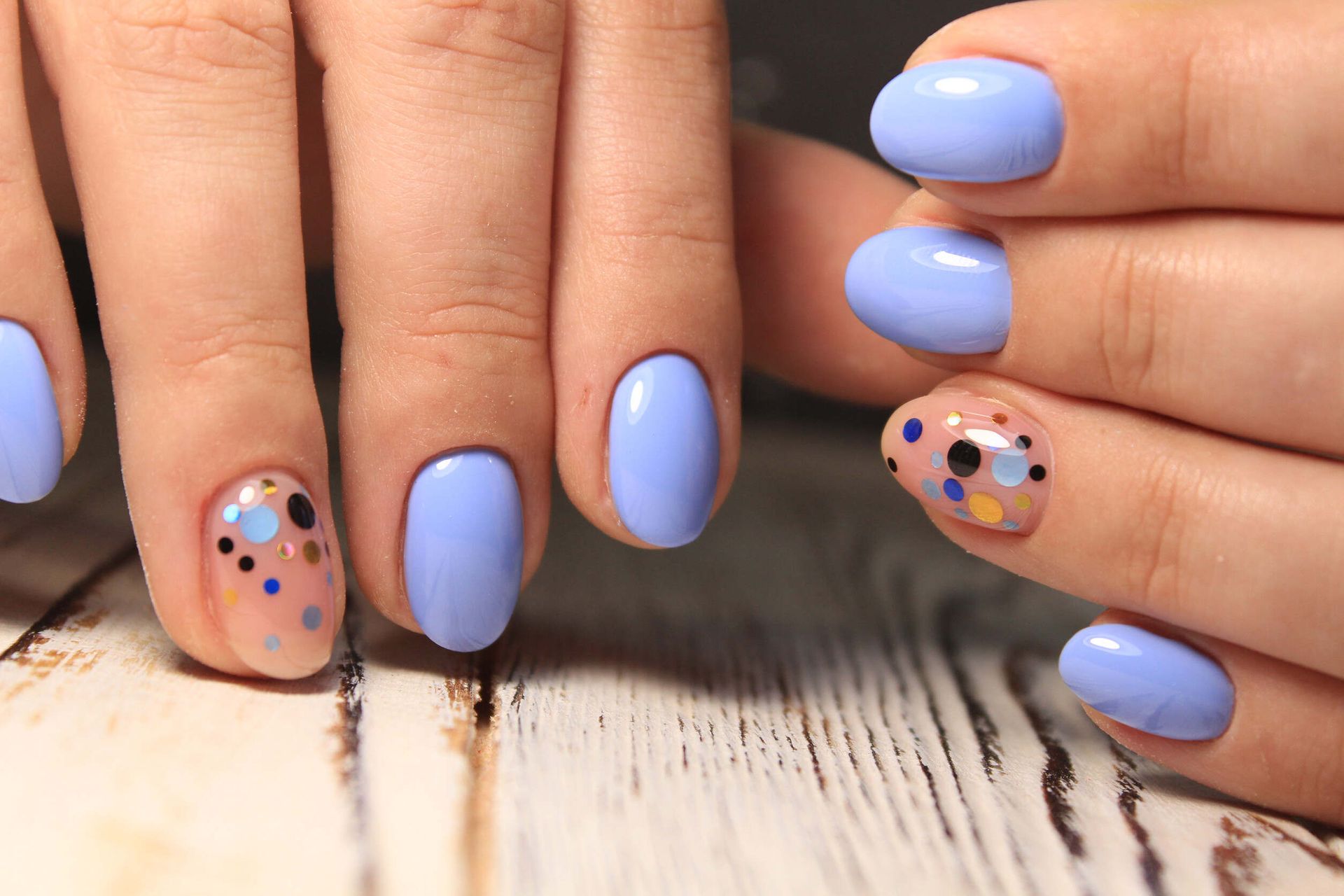 Un primer plano de las uñas de una mujer con esmalte de uñas azul sobre una mesa de madera.