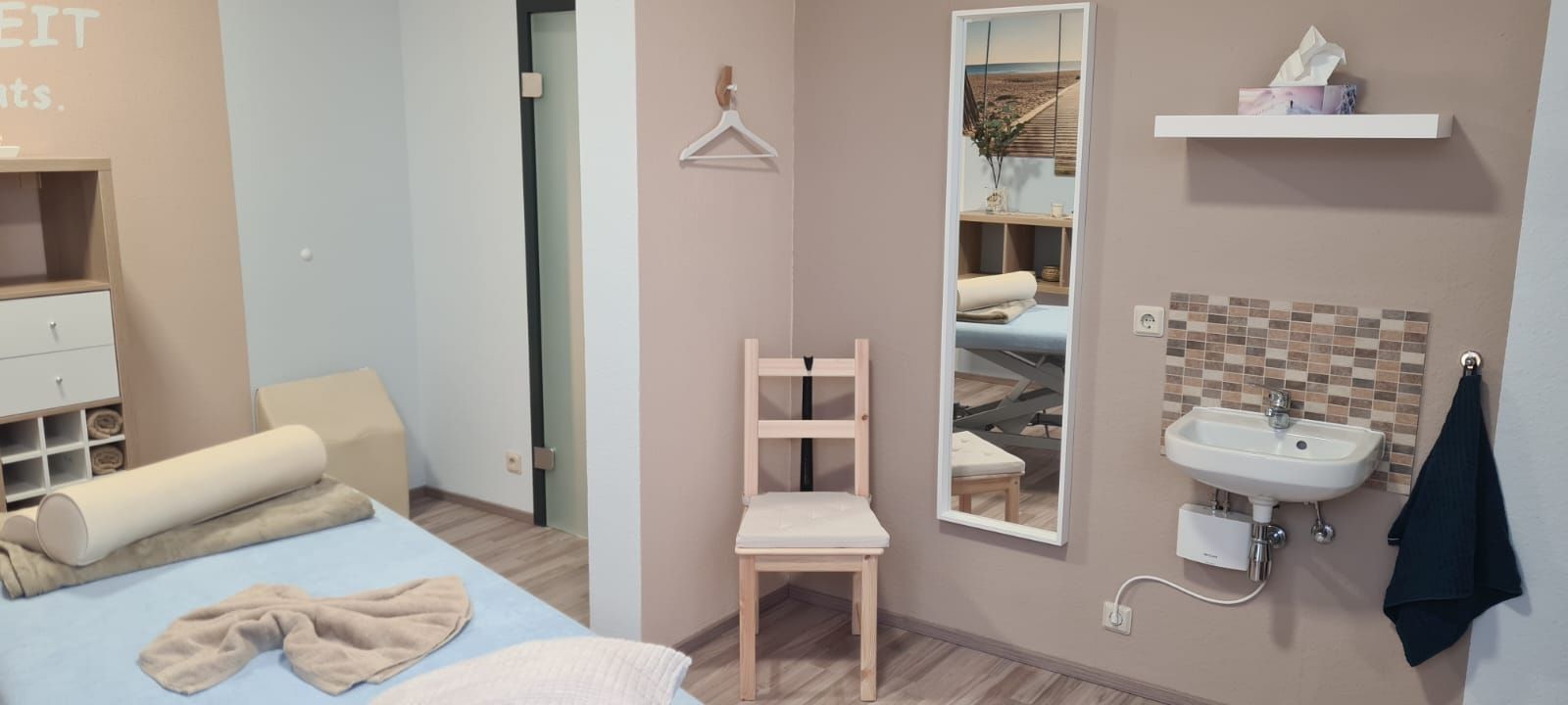 Ein Zimmer mit Bett, Stuhl, Spiegel und Waschbecken.