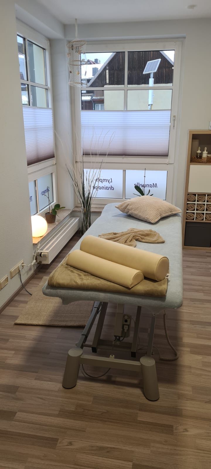 In einem Raum neben einem Fenster steht eine Massageliege.