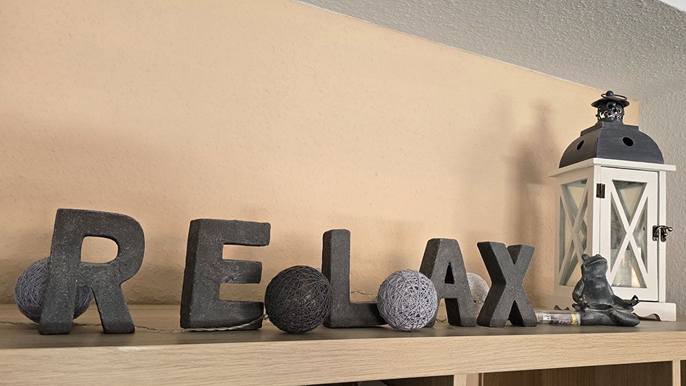 Das Wort „Relax“ steht in schwarzen Buchstaben auf einem Holzregal