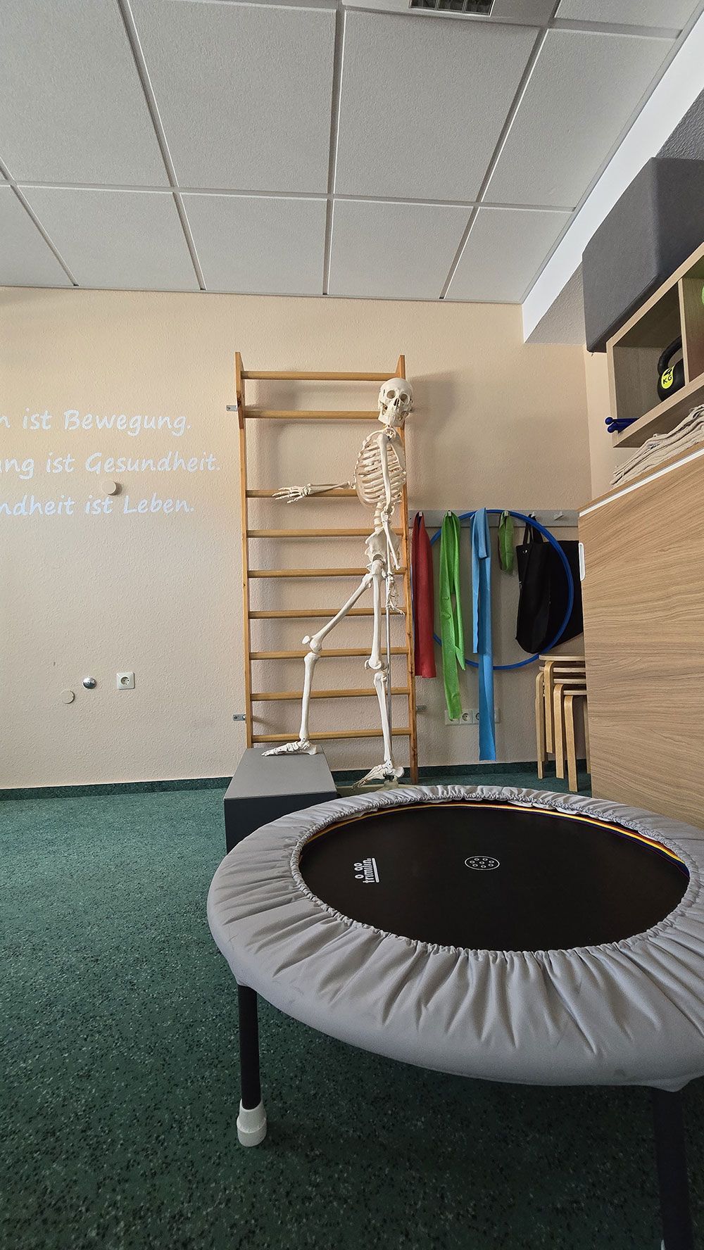 In einem Raum steht ein Trampolin neben einem Skelett.
