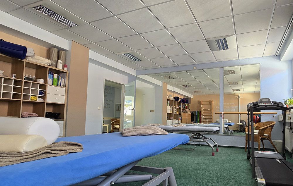 Ein Physiotherapieraum mit blauen Tischen und einem Laufband