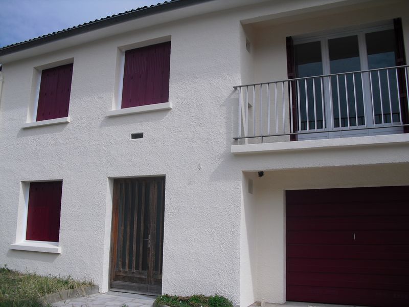 Maison blanche à deux étages avec volets violets, balcon et porte de garage