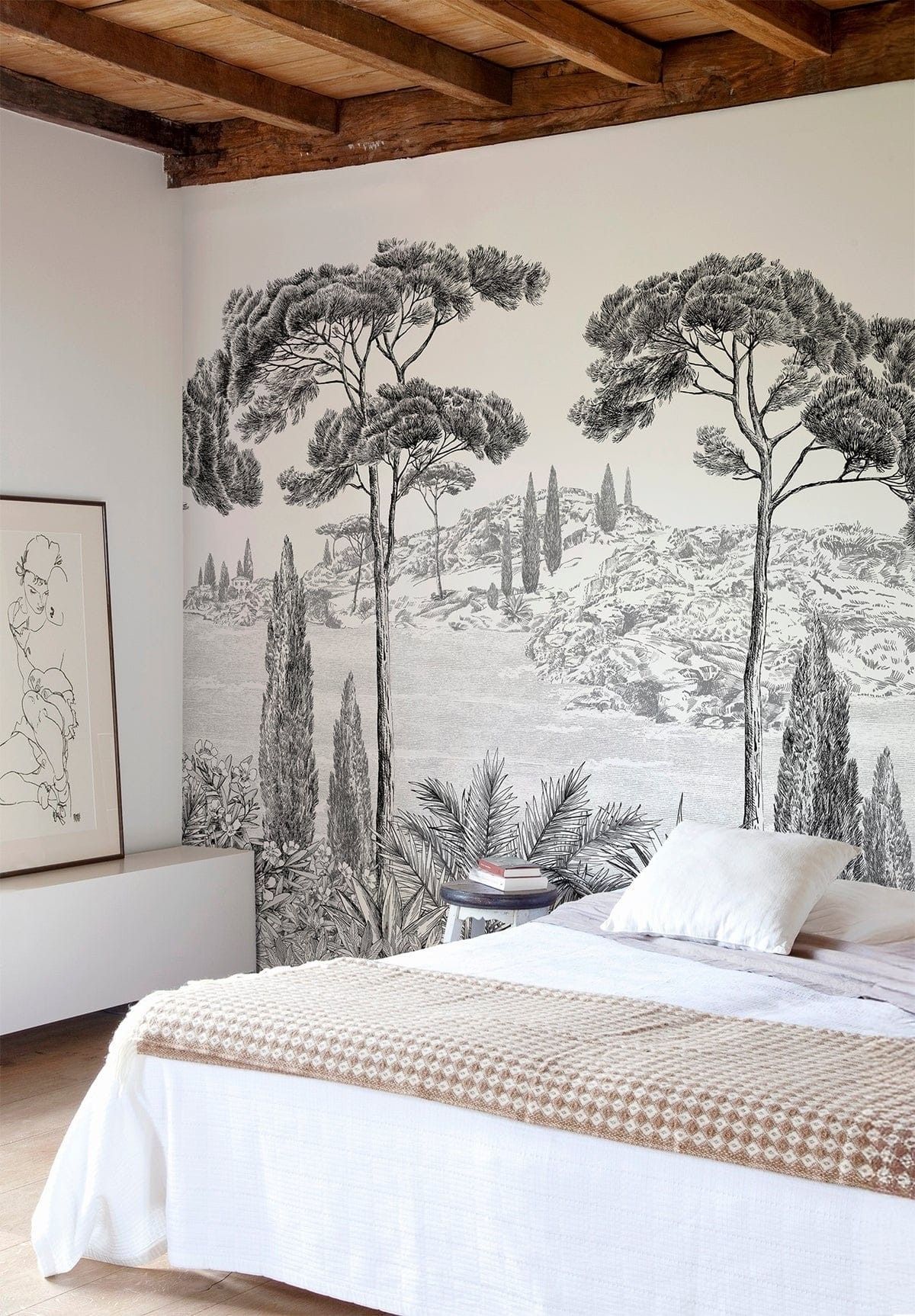Chambre avec une grande fresque murale en noir et blanc représentant un arbre derrière un lit aux draps blancs et au jeté tissé