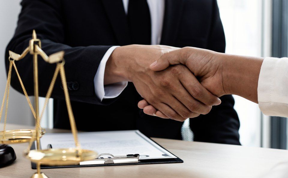 Ein Mann und eine Frau geben sich vor einer Waage der Gerechtigkeit die Hand.