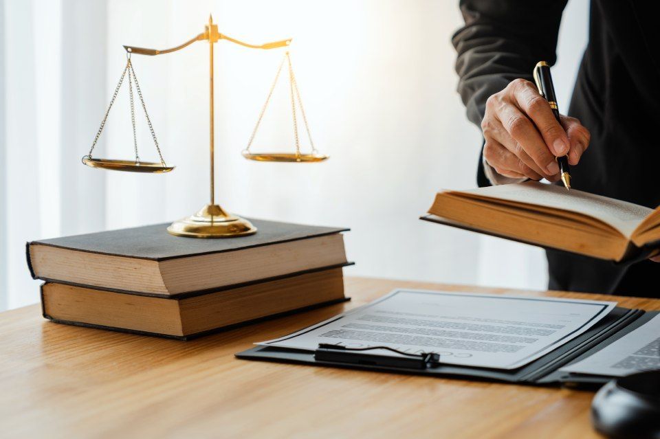 Ein Anwalt schreibt vor einer Waage der Gerechtigkeit auf ein Stück Papier.