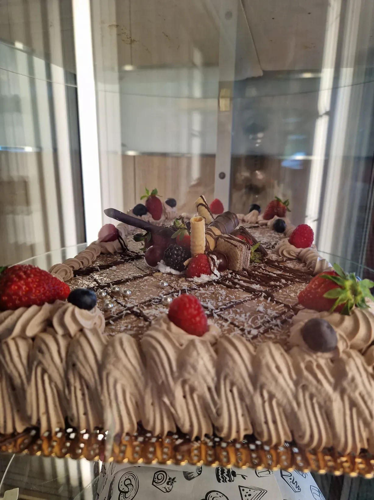 Pastel de chocolate con glaseado, fruta y decoraciones en vitrina.
