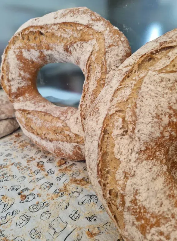 Primer plano de un pan rústico, uno de ellos en forma de anillo, espolvoreado con harina, sobre una superficie estampada.