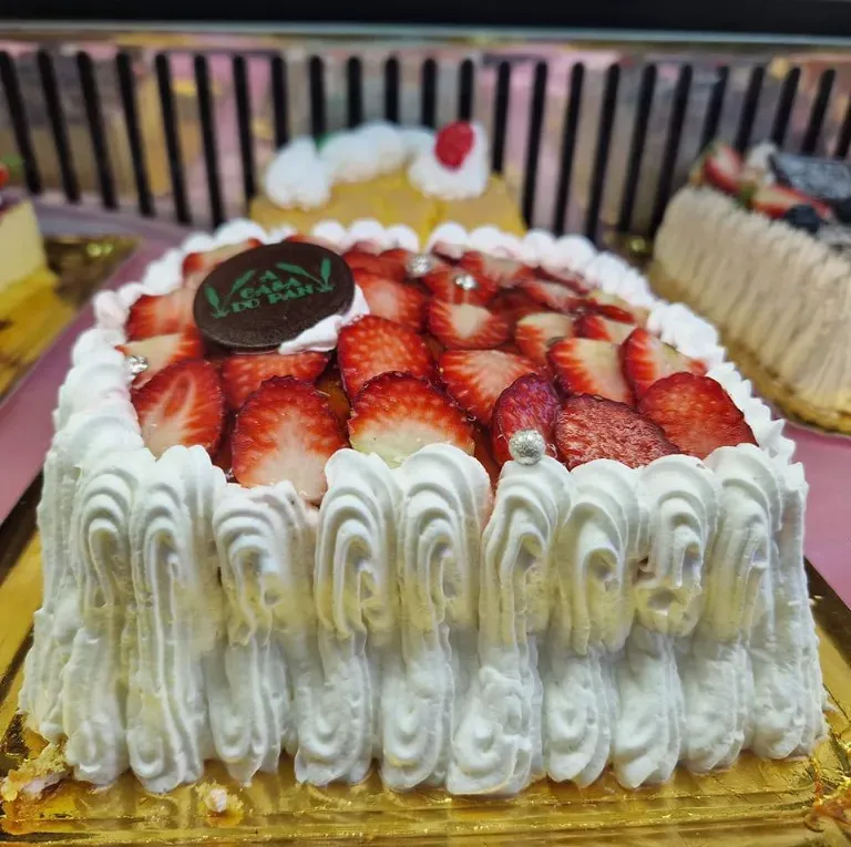 Pastel cuadrado con glaseado blanco, fresas y un emblema de chocolate.