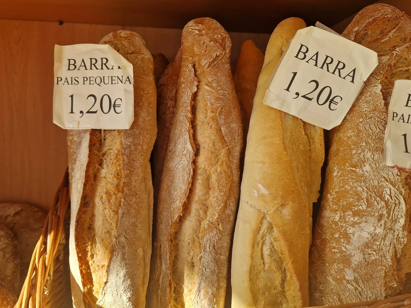Primer plano de varias hogazas de pan con etiquetas de precio en una panadería.