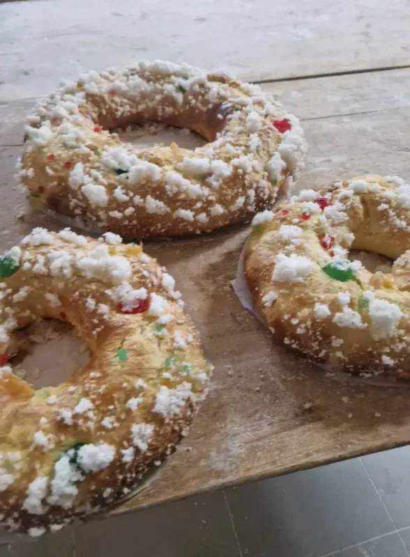 Tres pasteles en forma de anillo con cobertura blanca y frutas confitadas de colores sobre una superficie de madera.