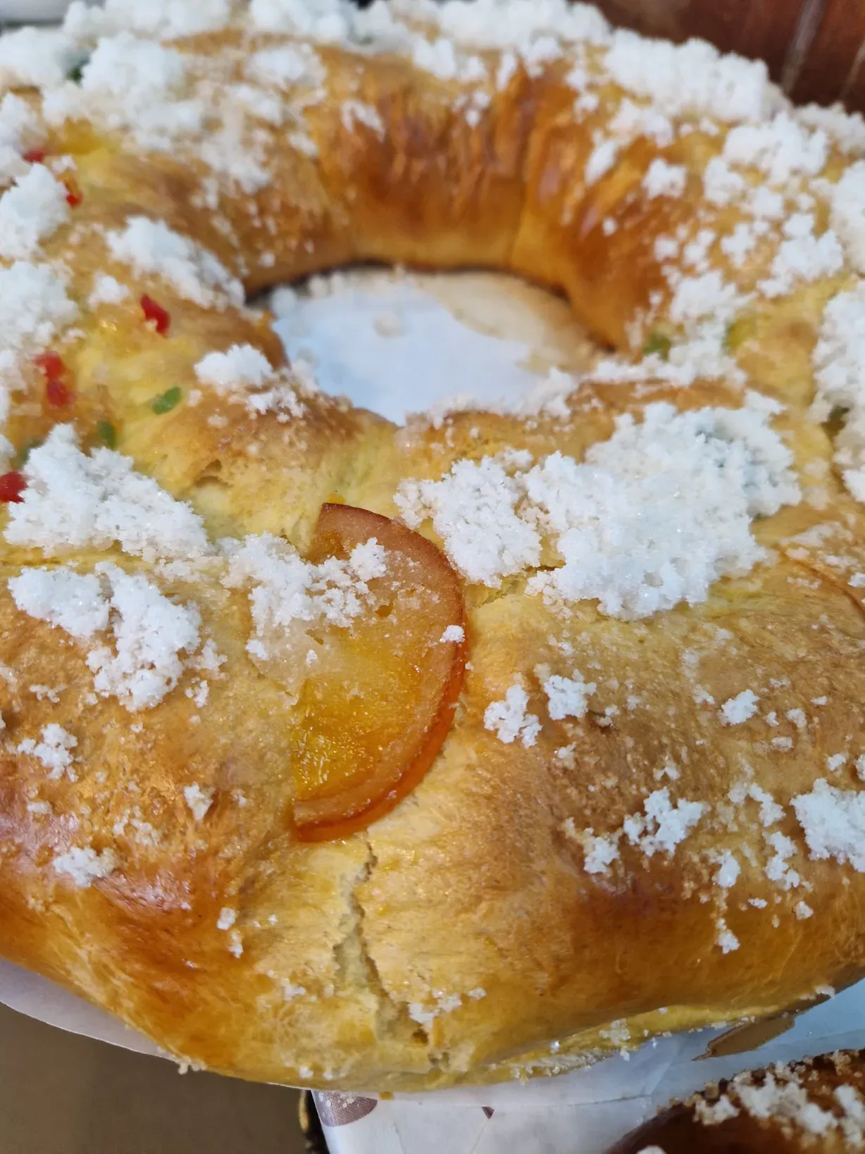 Masa brioche en forma de anillo, glaseada y espolvoreada con azúcar, decorada con fruta confitada.