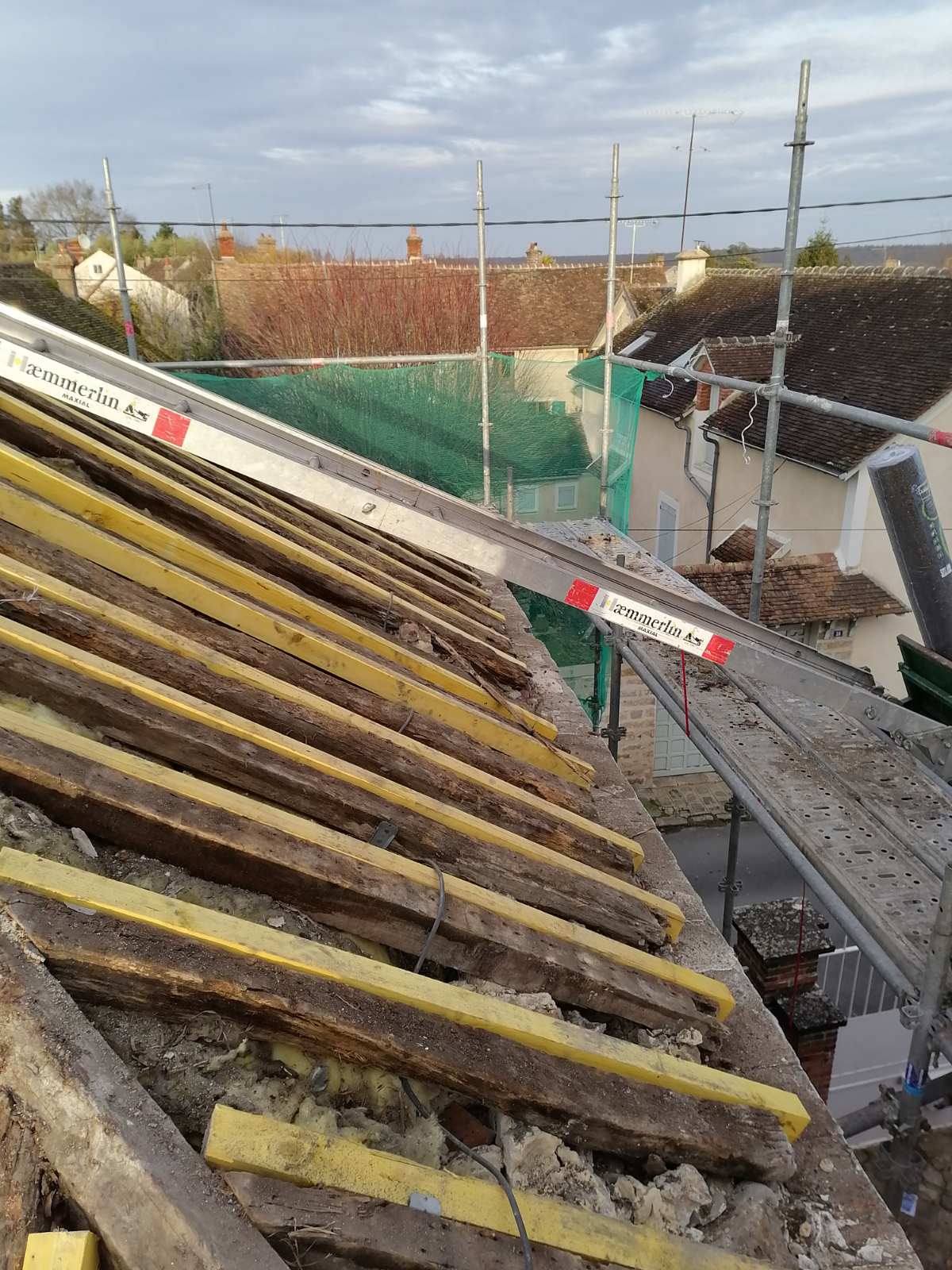 Toit en rénovation avec échelle appuyée entre un échafaudage et le lattage en bois de la toiture