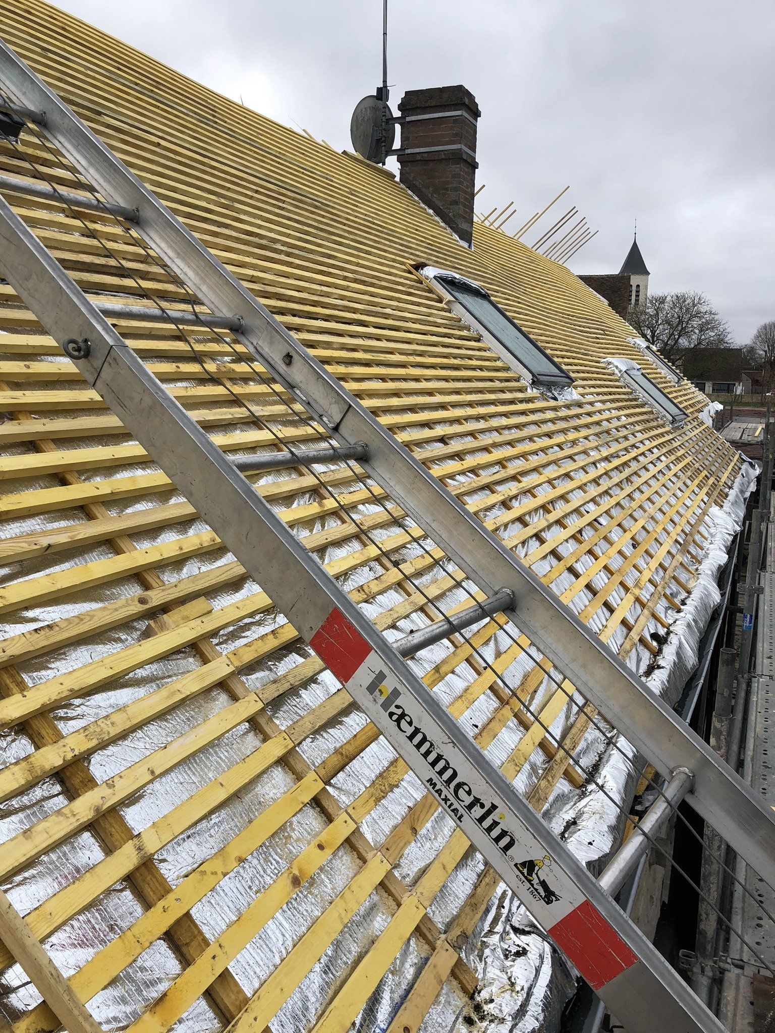 Toit en rénovation avec deux Velux, lattage en bois et échelle positionnée sur la surface