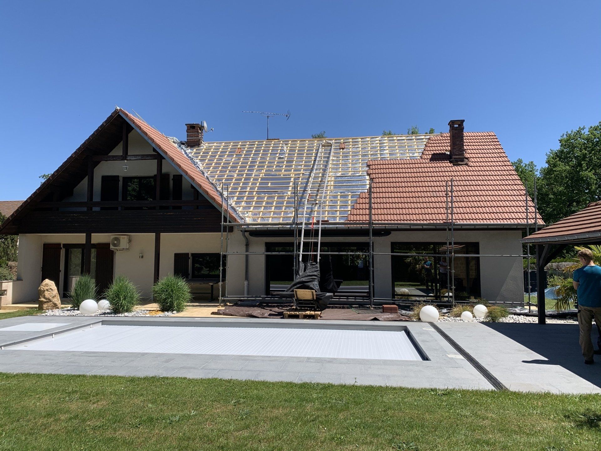 Maison avec toit en rénovation montrant la pose de tuile pratiquement terminée sur lattage en bois 